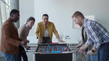 Genç, yakışıklı, çok ırklı iş adamları masa futbolu oynuyor ve ofiste dinleniyor.