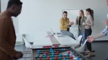 Genç, yakışıklı, çok ırklı iş adamları masa futbolu oynuyor ve ofiste dinleniyor.