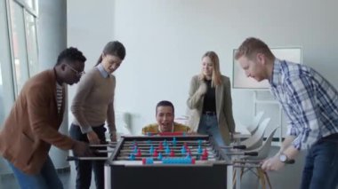 Genç, yakışıklı, çok ırklı iş adamları masa futbolu oynuyor ve ofiste dinleniyor.