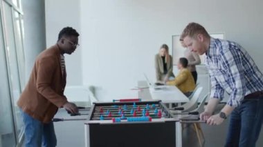 Genç, yakışıklı, çok ırklı iş adamları masa futbolu oynuyor ve ofiste dinleniyor.