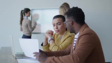 Yakışıklı Afrikalı genç iş adamı ve kısa saçlı kadın ofiste otururken dizüstü bilgisayarda çalışıyorlar.