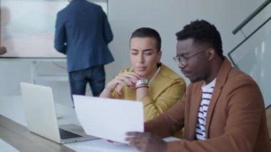 Yakışıklı Afrikalı genç iş adamı ve kısa saçlı kadın ofiste otururken dizüstü bilgisayarda çalışıyorlar.