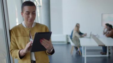 Genç kısa saçlı iş kadını ofiste dikiliyor ve takımının önünde dijital tablet kullanıyor.