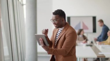 Yönetim kurulundaki iş arkadaşlarının önünde dijital tabletle çalışan yakışıklı Afrikalı genç bir iş adamı.