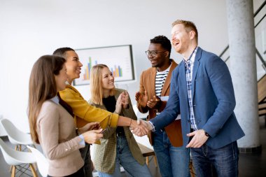 Genç yaratıcı ekip üyeleri modern ofiste çalışırken el sıkışıyor.