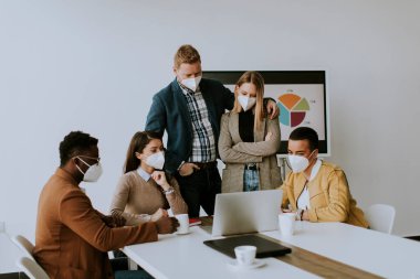 Çok ırklı iş adamlarından oluşan bir grup yüz koruma maskeleriyle birlikte çalışıyor ve ofiste yeni bir proje hazırlıyorlar.