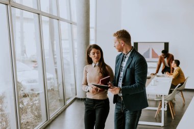 Genç girişimciler modern ofiste birlikte yürüyor ve dijital tablet kullanıyorlar.