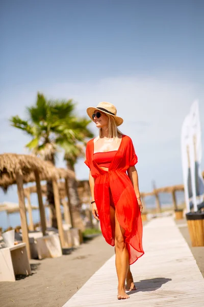 夏天穿着红衣服在海滩上散步的年轻漂亮的女人 — 图库照片