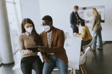 Yakışıklı Afrikalı genç iş adamı ve sevimli iş kadını yüz koruyucu maskeler takıp dijital tablet üzerinde çalışıyorlar.