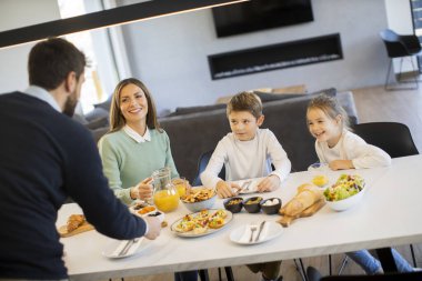 Genç mutlu aile, evdeki yemek masasında kahvaltı ederken konuşuyor.