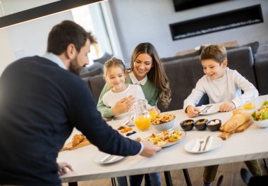 Genç mutlu aile, evdeki yemek masasında kahvaltı ederken konuşuyor.