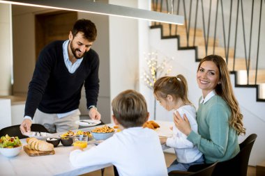 Genç mutlu aile, evdeki yemek masasında kahvaltı ederken konuşuyor.