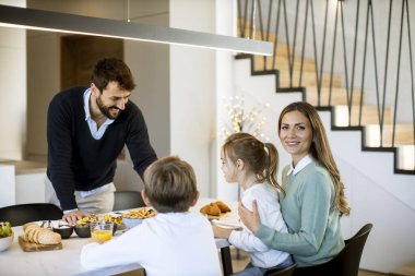 Genç mutlu aile, evdeki yemek masasında kahvaltı ederken konuşuyor.