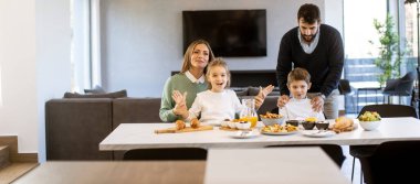 Genç mutlu aile, evdeki yemek masasında kahvaltı ederken konuşuyor.