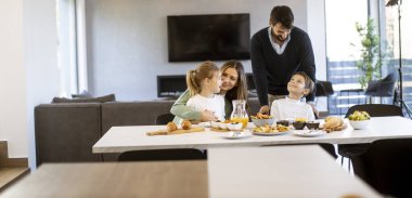 Genç mutlu aile, evdeki yemek masasında kahvaltı ederken konuşuyor.