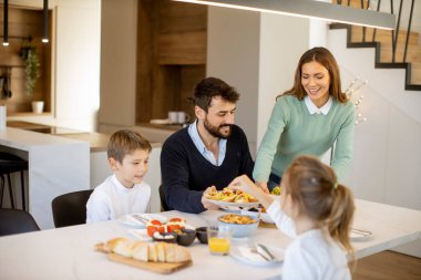 Genç mutlu aile, evdeki yemek masasında kahvaltı ederken konuşuyor.