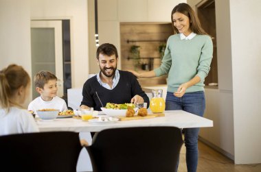 Genç anne modern mutfakta ailesine kahvaltı hazırlıyor.