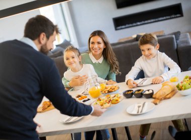 Genç mutlu aile, evdeki yemek masasında kahvaltı ederken konuşuyor.