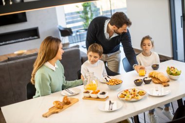 Genç mutlu aile, evdeki yemek masasında kahvaltı ederken konuşuyor.