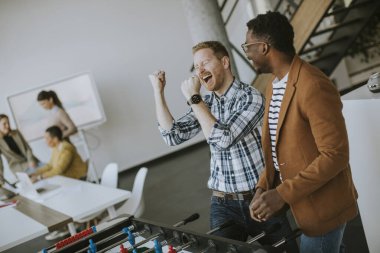 Genç, yakışıklı, çok ırklı iş adamları masa futbolu oynuyor ve ofiste dinleniyor.