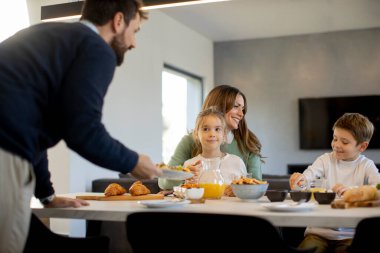 Genç mutlu aile, evdeki yemek masasında kahvaltı ederken konuşuyor.