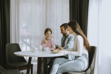 Genç ve mutlu bir aile kek yer ve odada çay içer.