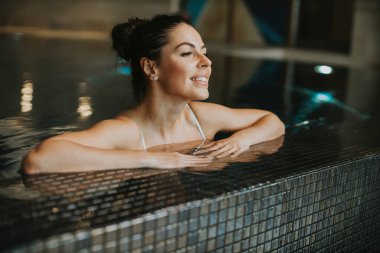 Kapalı yüzme havuzunun havuz kenarında dinlenen güzel genç bir kadın.