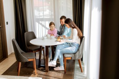 Genç ve mutlu bir aile kek yer ve odada çay içer.