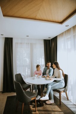 Genç ve mutlu bir aile kek yer ve odada çay içer.