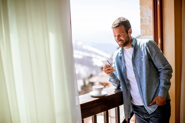 Kjekk Ung Mann Som Bruker Mobiltelefon Med Kopp Vintervinduet – stockfoto