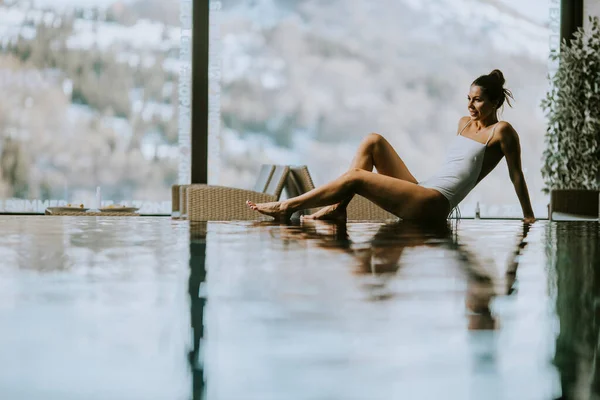 Pretty young woman relaxing on the poolside of infinity swimming pool at winter time