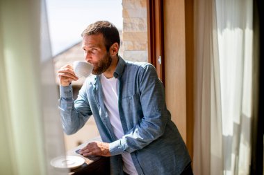 Kışın penceresinde bir fincan sıcak çayla yakışıklı genç bir adam.