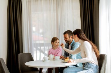 Genç ve mutlu bir aile kek yer ve odada çay içer.