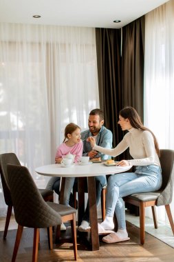 Genç ve mutlu bir aile kek yer ve odada çay içer.