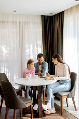 Genç ve mutlu bir aile kek yer ve odada çay içer.