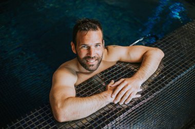 Yüzme havuzunda rahatlayan yakışıklı, gülümseyen genç adamın portresi