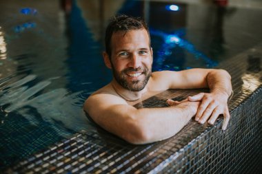 Yüzme havuzunda rahatlayan yakışıklı, gülümseyen genç adamın portresi