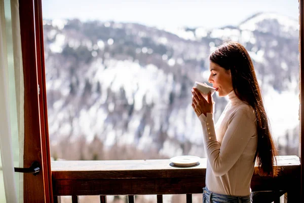 Kışın penceresinde bir fincan sıcak çayla güzel genç bir kadın.