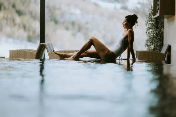 Pretty young woman relaxing on the poolside of infinity swimming pool at winter time