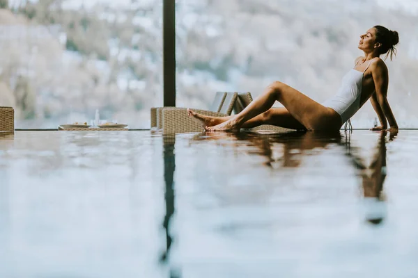 冬天的时候 漂亮的年轻女子在无限大的游泳池边休息 — 图库照片