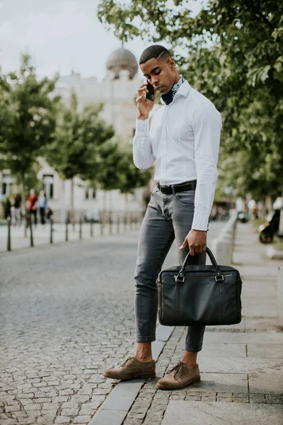 Yakışıklı Afro-Amerikan iş adamı sokakta taksi beklerken cep telefonu kullanıyor.