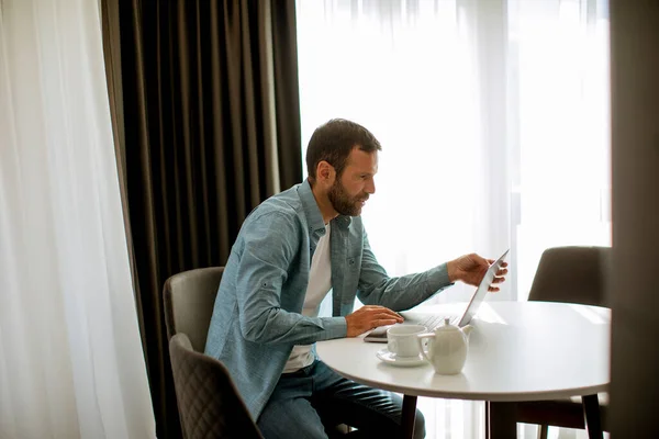 一个英俊的年轻人在客厅里用笔记本电脑喝茶 — 图库照片
