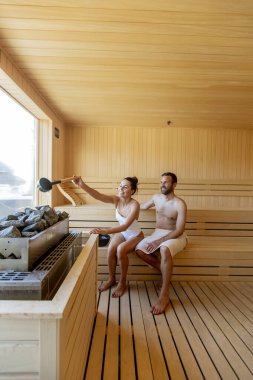 Yakışıklı genç çift saunada dinleniyor ve pencereden kış ormanlarını izliyorlar.