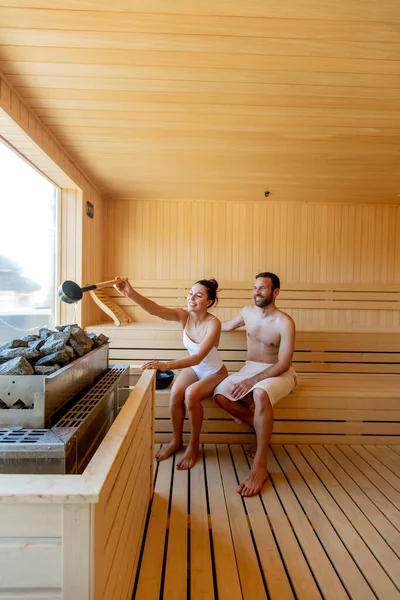 Yakışıklı genç çift saunada dinleniyor ve pencereden kış ormanlarını izliyorlar.