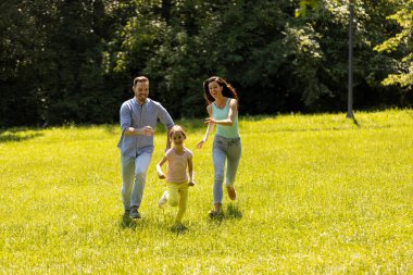 Güneşli bir günde parkta koşan küçük tatlı kızıyla mutlu bir aile.