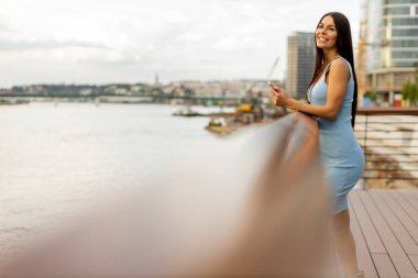 Güzel genç bayan nehir kenarında dururken cep telefonu kullanıyor.