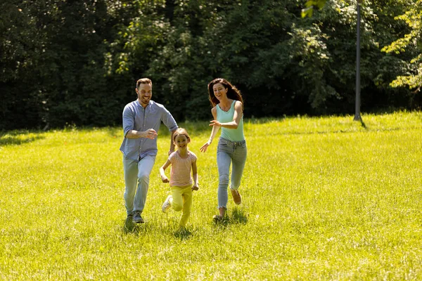 晴れた日に公園を走っているかわいい娘と幸せな若い家族 — ストック写真