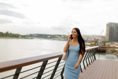 Nehir kenarında yürürken cep telefonu kullanan genç ve güzel bir kadın.