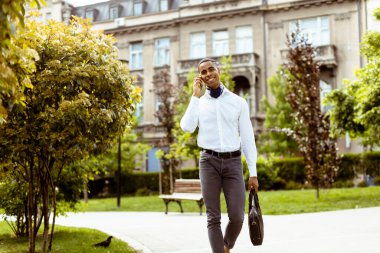 Yakışıklı Afro-Amerikan iş adamı sokakta yürürken cep telefonu kullanıyor.