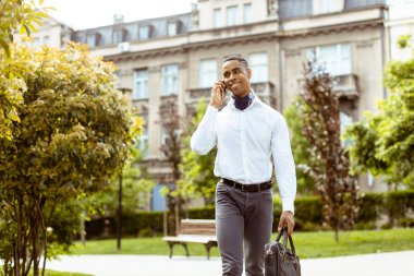 Yakışıklı Afro-Amerikan iş adamı sokakta yürürken cep telefonu kullanıyor.